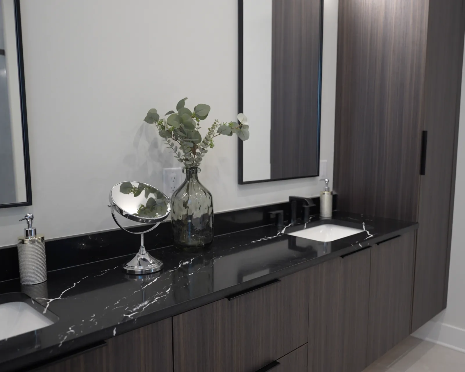 Double bathroom vanity with dark cabinets, black stone countertop, and mirrors