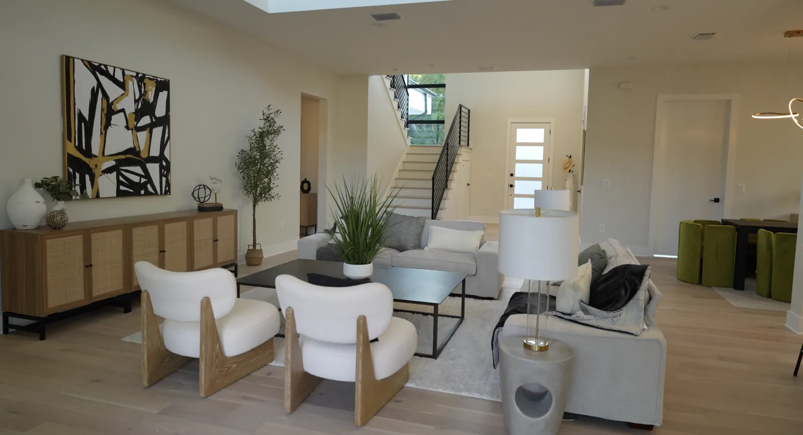 Open-plan living room with white chairs, gray sofas, and a staircase